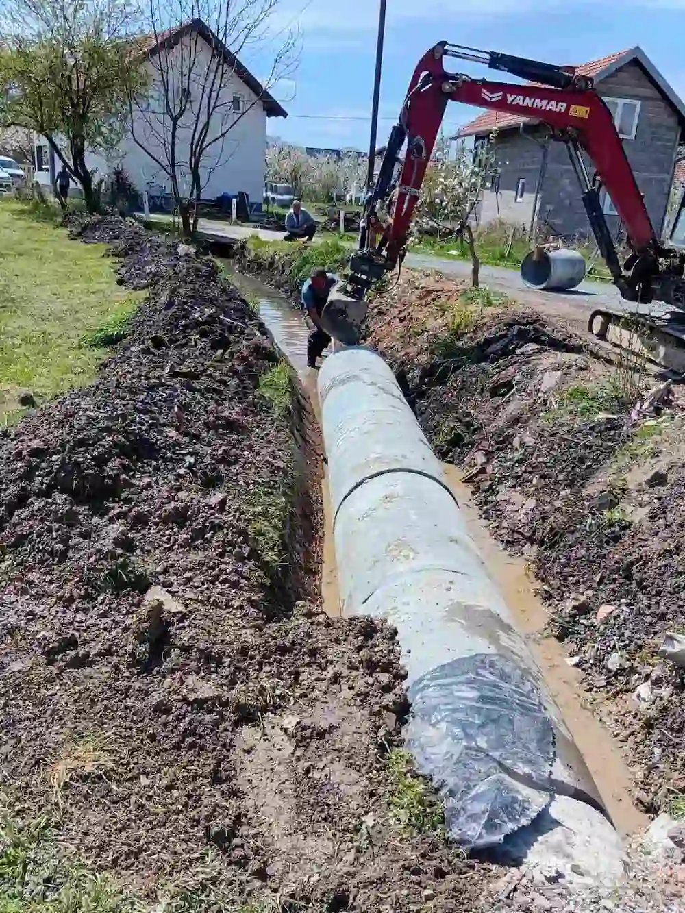Yanmar bager postavlja betonske kanalizacione cijevi u rov